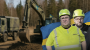 Två b byggnadsarbetare som står framför en AI-genererad bild på en militärfärgad kan med svenska flaggor på